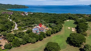 Aerial view of Casa Aguasalada, showcasing the modern design, infinity pool, and lush tropical surroundings with views of the golf course and nearby beach.