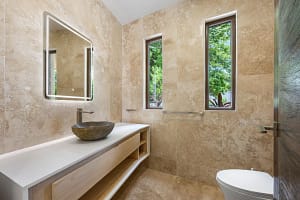Elegant en-suite bathroom at Casa Manta Ray featuring travertine floors, stone sinks, and ocean-view rain showers.