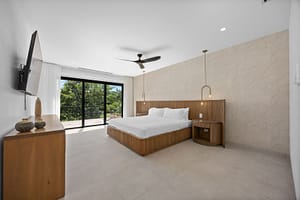 Elegant bedroom in Casa Aguasalada, featuring a plush king-size bed, teak accents, and floor-to-ceiling windows with tropical views.