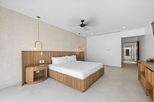 Elegant bedroom in Casa Aguasalada, featuring a plush king-size bed, teak accents, and floor-to-ceiling windows with tropical views.