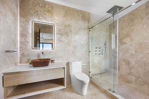 Elegant en-suite bathroom at Casa Manta Ray featuring travertine floors, stone sinks, and ocean-view rain showers.