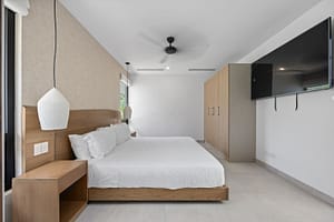 Elegant bedroom in Casa Aguasalada, featuring a plush king-size bed, teak accents, and floor-to-ceiling windows with tropical views.