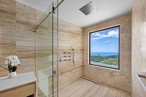 Elegant en-suite bathroom at Casa Manta Ray featuring travertine floors, stone sinks, and ocean-view rain showers.
