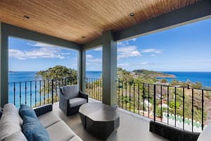 Luxurious ocean-view balcony with glass railings, outdoor seating, and breathtaking panoramic views of Flamingo Marina and the Pacific Ocean.