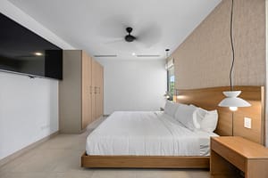 Elegant bedroom in Casa Aguasalada, featuring a plush king-size bed, teak accents, and floor-to-ceiling windows with tropical views.