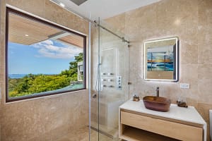 Elegant en-suite bathroom at Casa Manta Ray featuring travertine floors, stone sinks, and ocean-view rain showers.