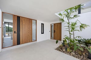 Modern teak entrance door of Casa Aguasalada, featuring sleek vertical wood panels and a contemporary handle, set against lush tropical landscaping.