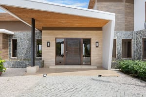 Grand entrance of Casa Seahorse featuring elegant stone accents, custom wood doors, and warm ambient lighting in Mar Vista, Playa Flamingo.