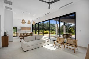Spacious and modern living room in Casa Aguasalada, featuring elegant teak accents, plush seating, and floor-to-ceiling windows with tropical views.