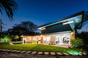 Stunning nighttime view of the front of Casa Kenya, featuring elegant lighting, modern tropical architecture, and lush landscaping in Hacienda Pinilla, Costa Rica.