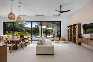 Spacious and modern living room in Casa Aguasalada, featuring elegant teak accents, plush seating, and floor-to-ceiling windows with tropical views.