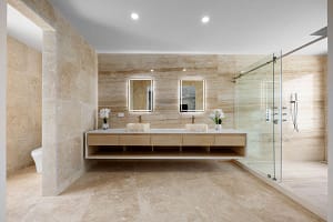Elegant en-suite bathroom at Casa Manta Ray featuring travertine floors, stone sinks, and ocean-view rain showers.
