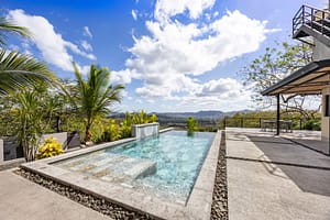 Luxurious infinity-edge pool with a cascading waterfall, surrounded by lush tropical gardens and stunning mountain views.