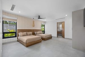 Elegant bedroom in Casa Aguasalada, featuring a plush king-size bed, teak accents, and floor-to-ceiling windows with tropical views.