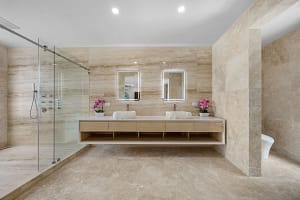Elegant en-suite bathroom at Casa Manta Ray featuring travertine floors, stone sinks, and ocean-view rain showers.