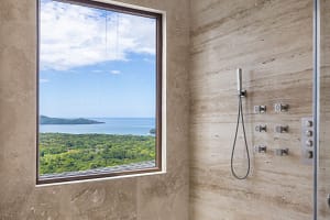 Luxurious bathroom at Casa Manta Ray with a rain shower and stunning Pacific Ocean views through large windows.